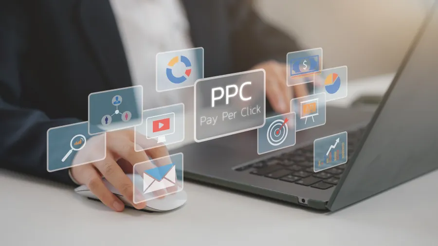 Person using laptop and mouse with floating PPC pay-per-click digital marketing icons above the keyboard.