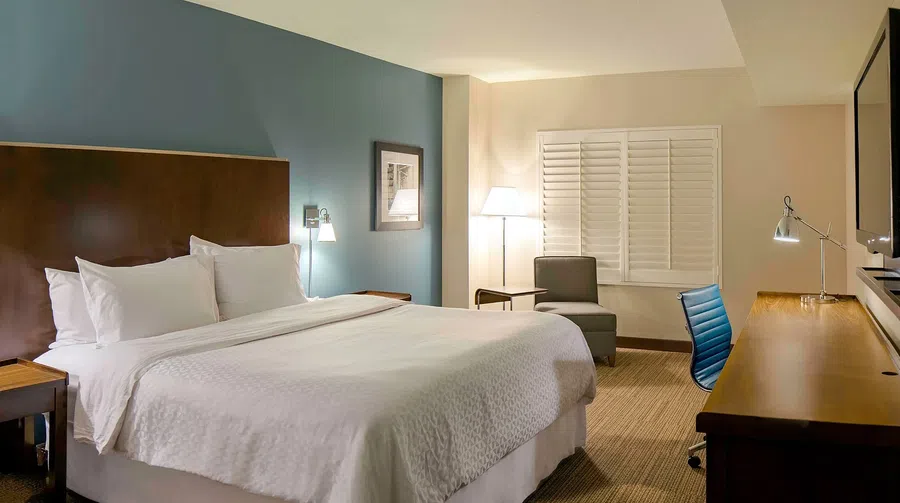 Modern hotel room with king-size bed, blue accent wall, wooden desk, chair, and soft lighting.