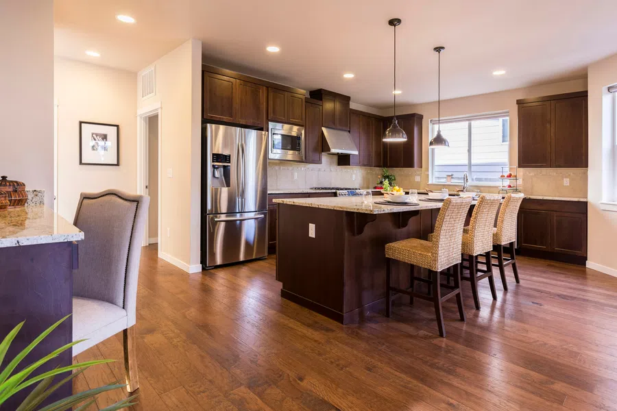 Modern kitchen with dark wood cabinets, stainless steel appliances, granite island, and wicker bar stools on hardwood floor