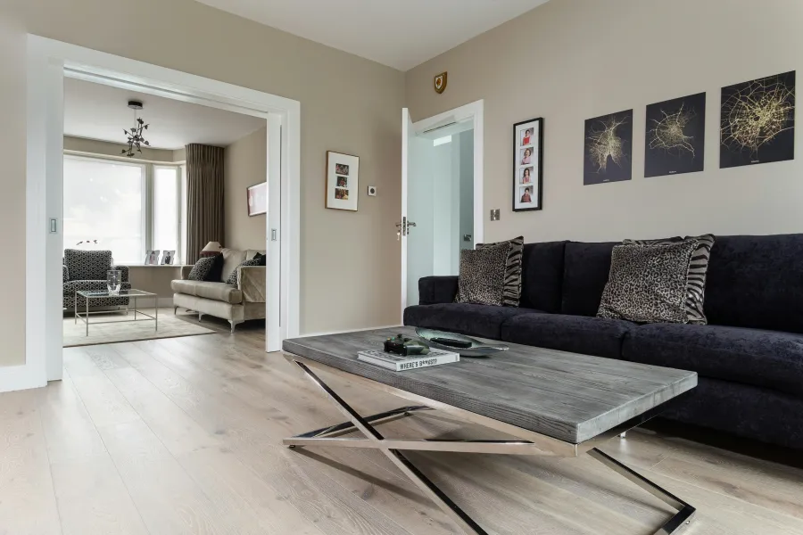 Modern living room with black sofa, wooden coffee table, leopard print pillows, and connected seating area with window.