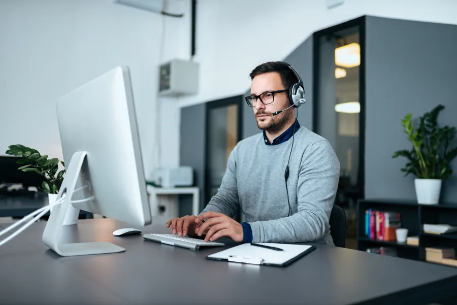 a man wearing headphones and sitting at a desk with a computer