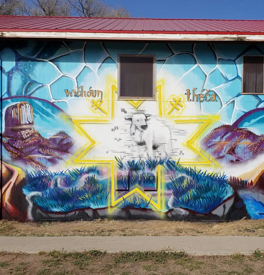 Colorful mural on wall featuring a white bull inside a yellow star with nature and tribal elements.