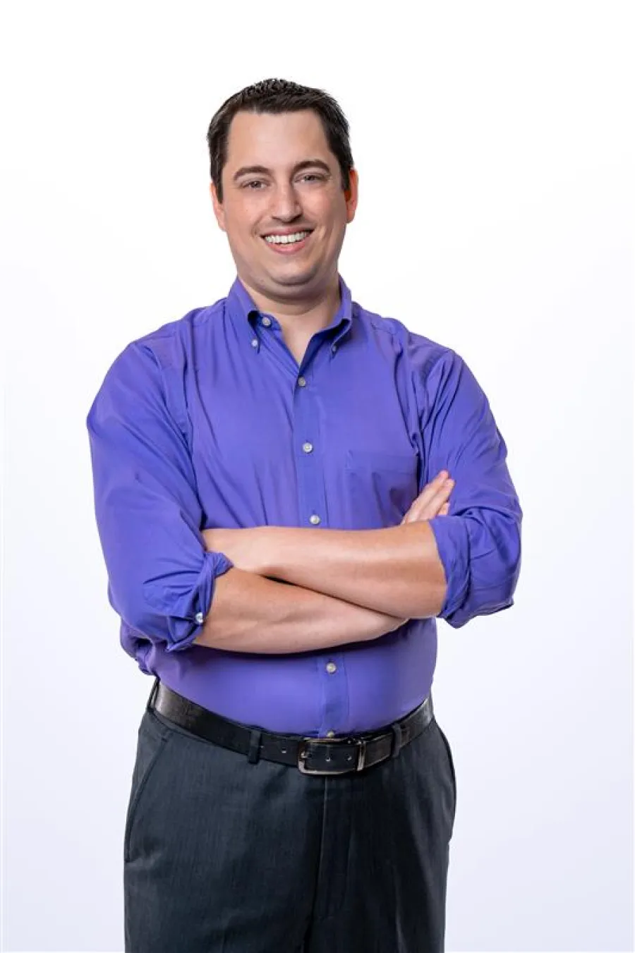 Smiling man in a purple shirt with rolled sleeves standing with arms crossed on a white background
