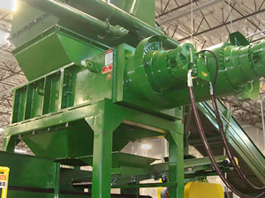 Large green industrial machine with conveyor belt and hoses inside factory warehouse setting