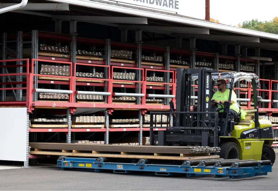 Forklift transporting metal materials in an outdoor warehouse with organized shelving racks labeled A to D
