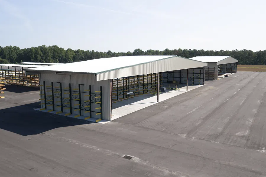 Large open-sided metal storage buildings with racks on spacious paved lot under clear sky.