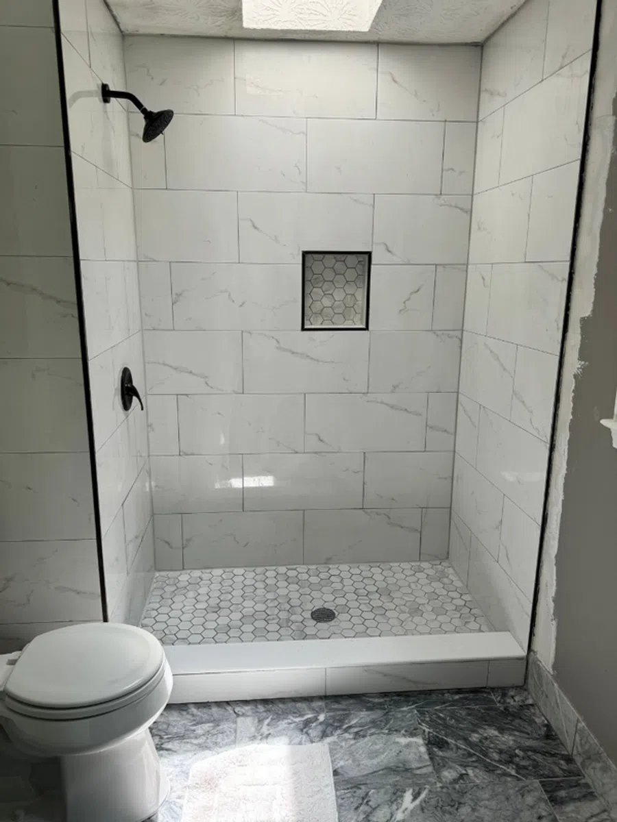Modern walk-in shower with white marble tiles and hexagon floor tiles next to a white toilet.