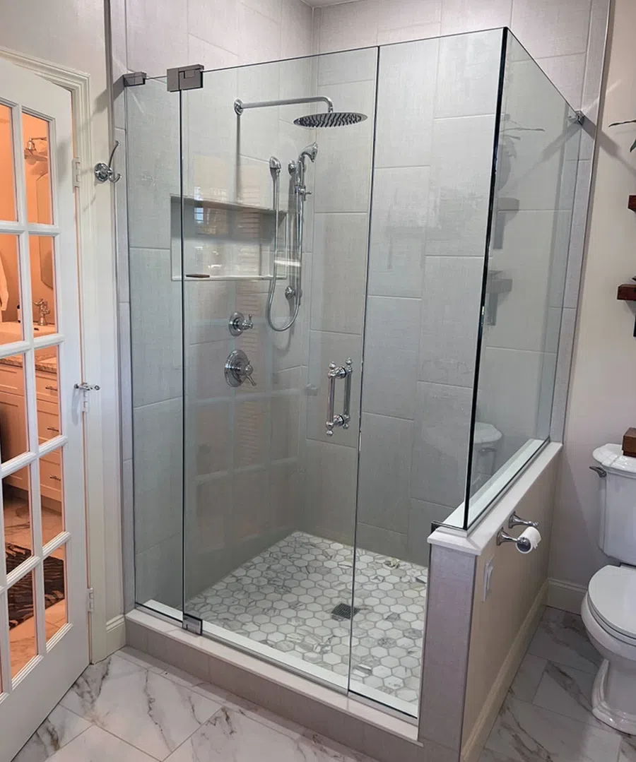 Modern glass shower enclosure with hexagonal tile floor and rain showerhead in a bright bathroom