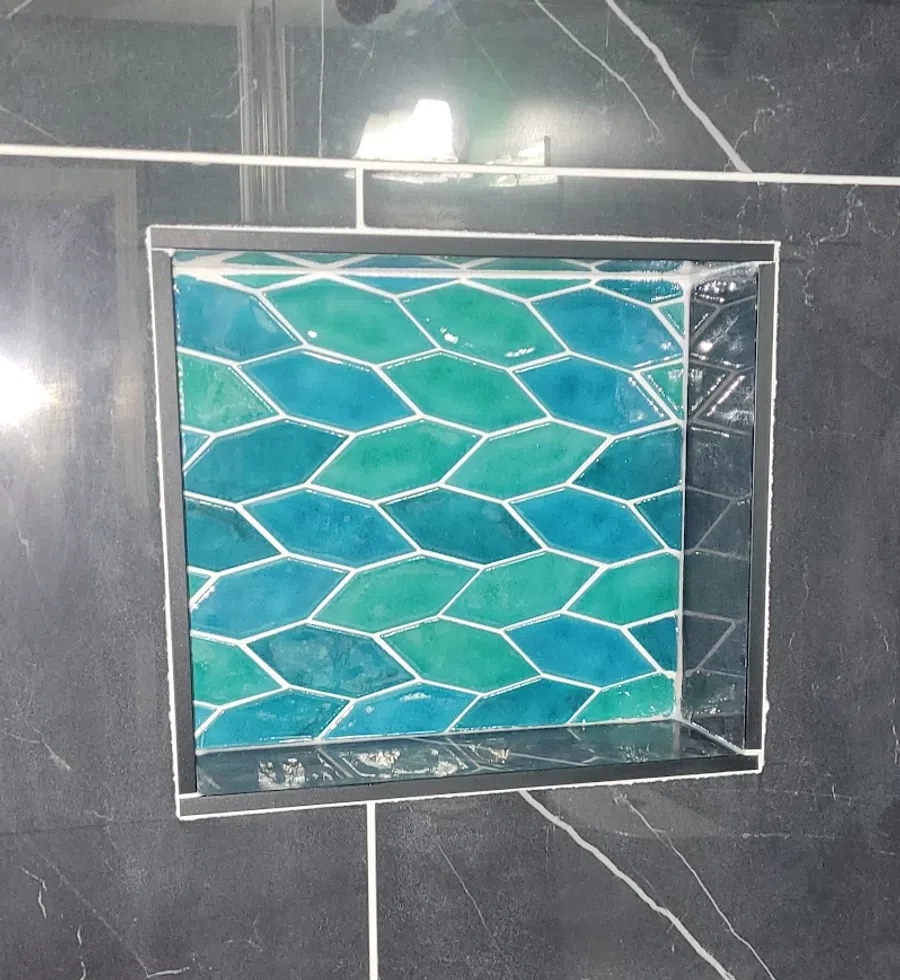 Bathroom shower niche with blue and green hexagonal tiles surrounded by black marble wall tiles with white veins