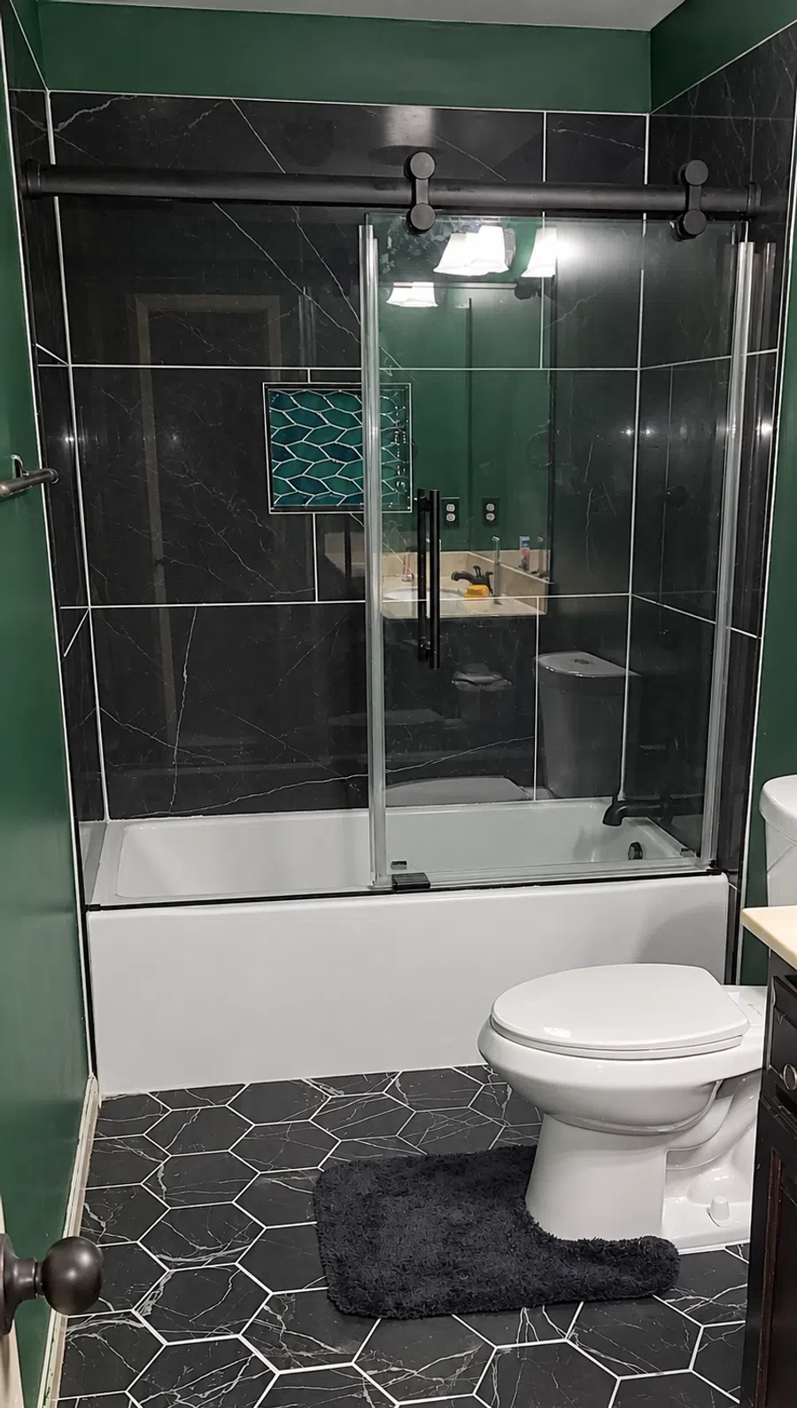 Modern bathroom with black hexagonal floor tiles, glass shower door, white toilet, and green walls.