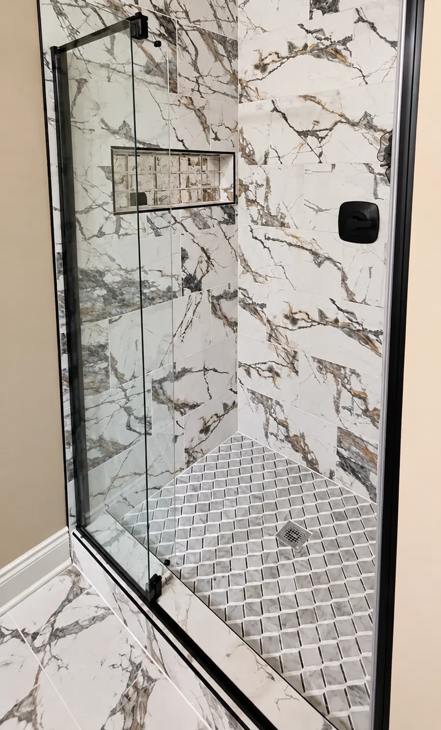 Modern shower with black frame glass door, gold rain shower head, and marble tile walls with beige grout.
