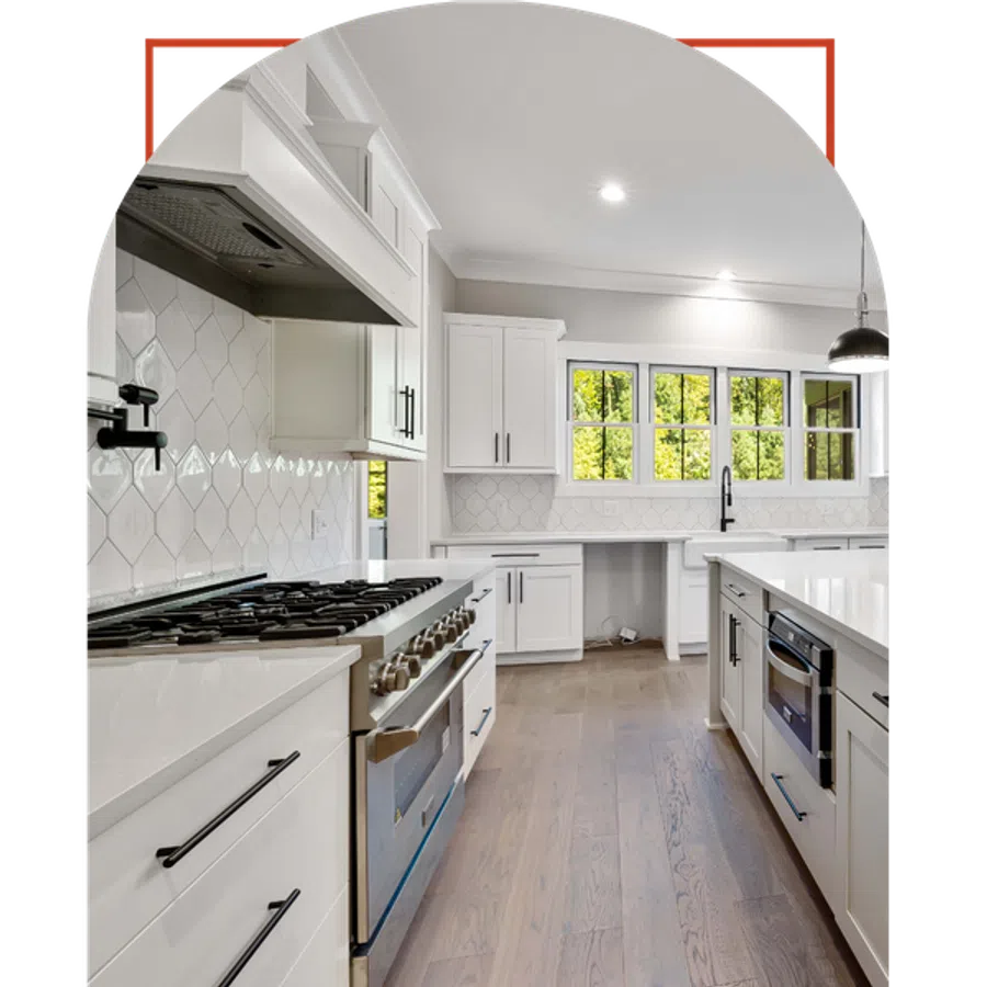 Modern white kitchen with stainless steel appliances, hardwood floors, and large windows letting in natural light