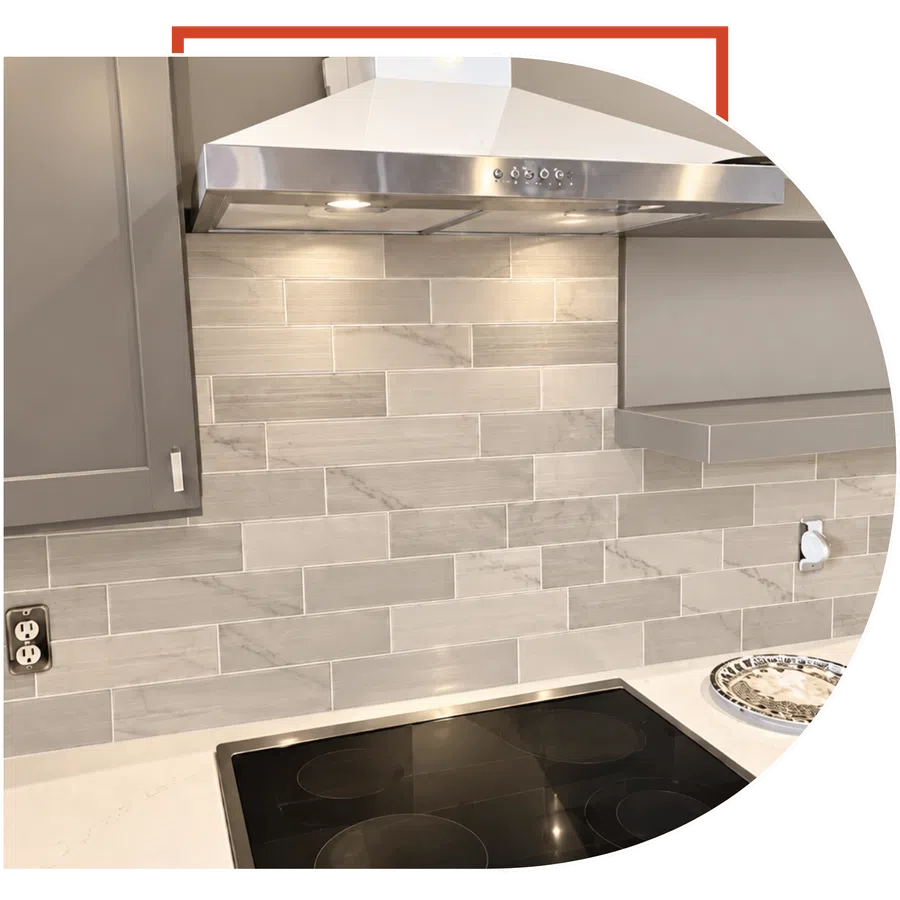 Modern kitchen stovetop with black glass cooktop, stainless steel hood, and beige subway tile backsplash.