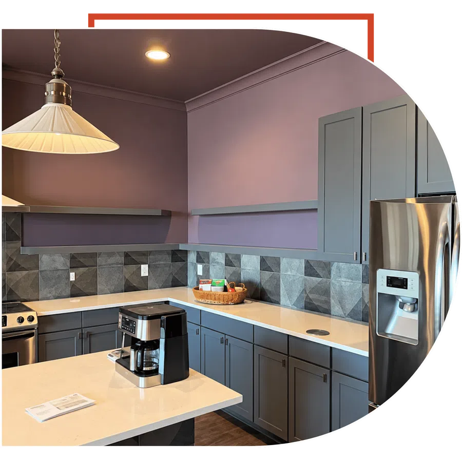 Modern kitchen with gray cabinets, geometric tile backsplash, stainless steel appliances, and coffee maker on island countertop