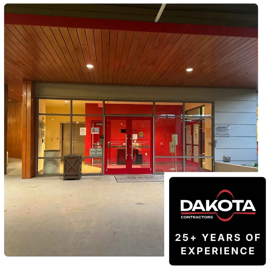 Modern building entrance with red doors and glass panels under a wooden ceiling with recessed lights.