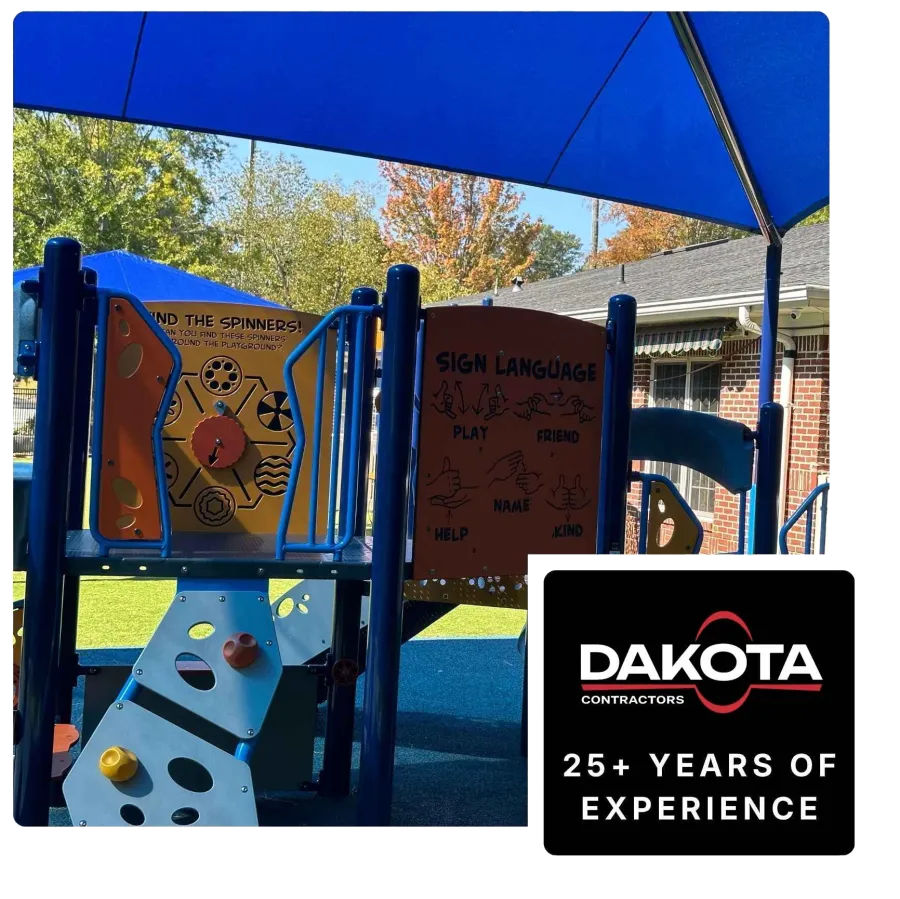 Children's playground with blue shade, sign language panel, and play equipment under a sunny sky.