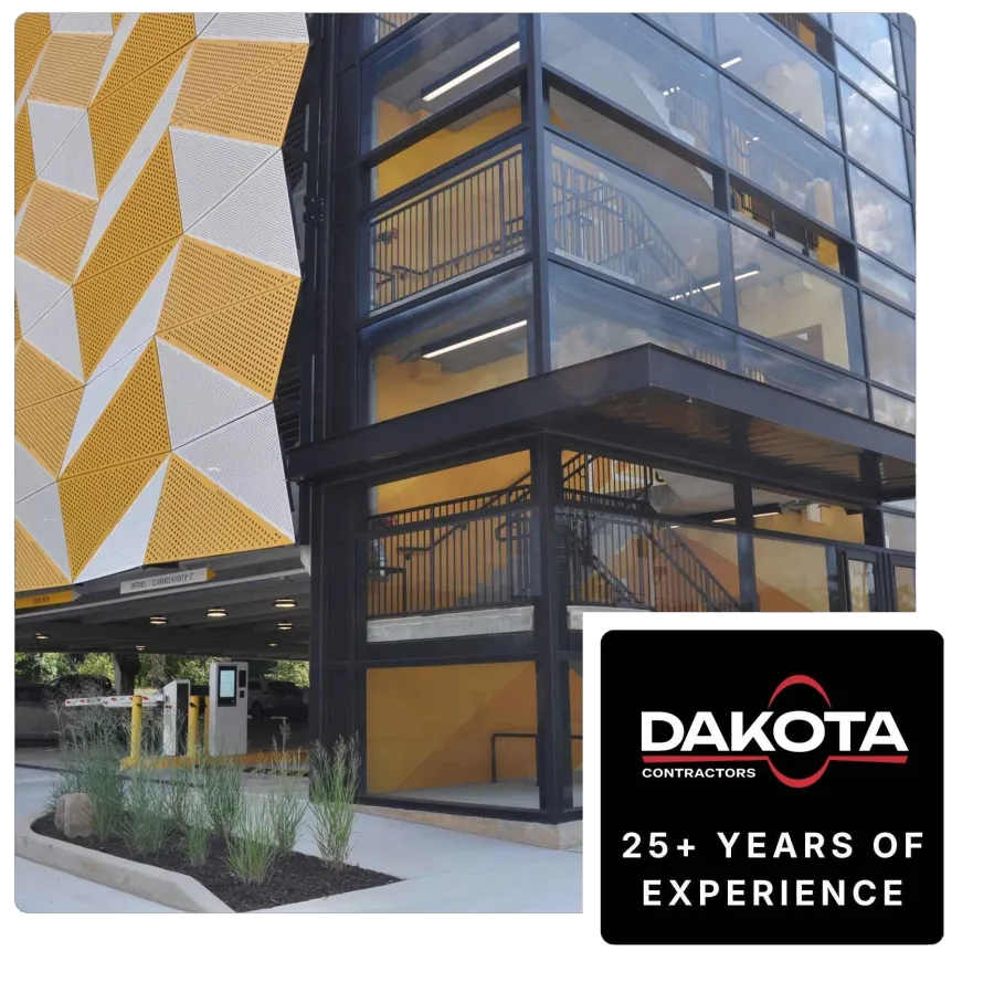 Modern building exterior with yellow and white geometric panels and a glass stairwell beside landscaped greenery.