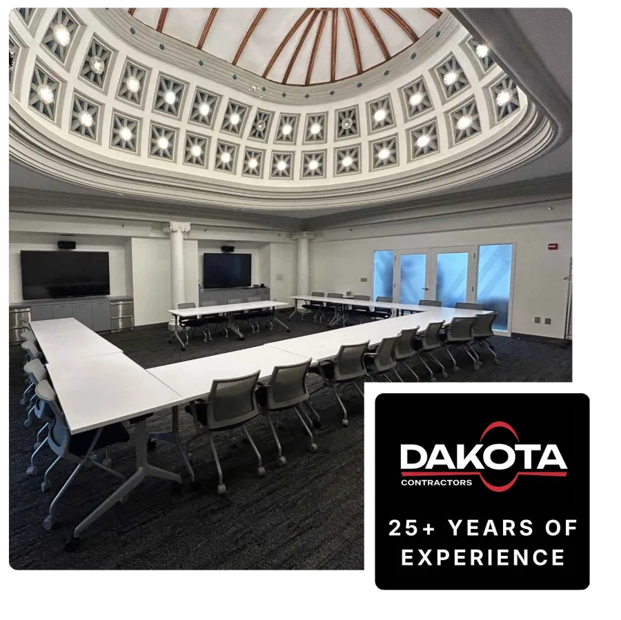 Modern conference room with U-shaped white tables, black chairs, dual monitors, and decorative domed ceiling lights.