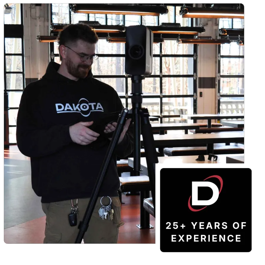 Man in Dakota hoodie using tech device on tripod inside a modern industrial space with large windows.