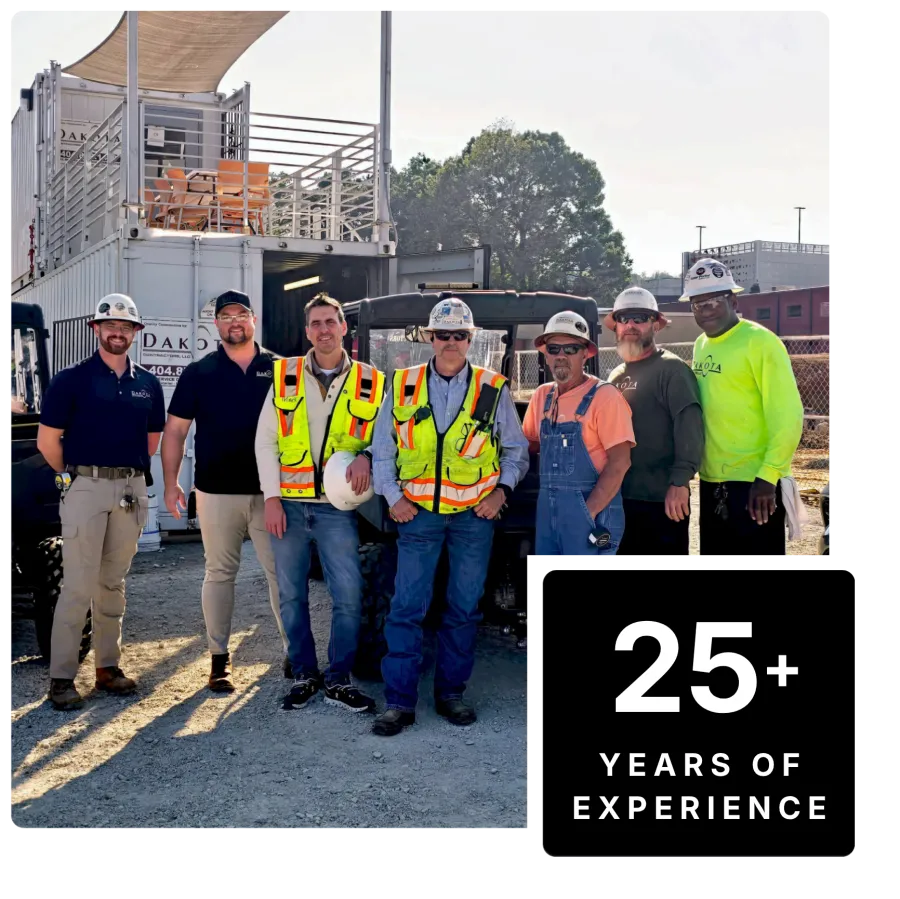 Group of construction workers wearing safety gear standing outdoors on a job site with equipment behind them.