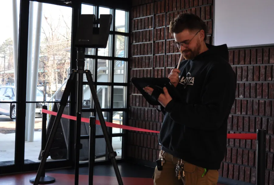 Man wearing glasses working on a tablet device next to tripod-mounted equipment inside a building lobby.