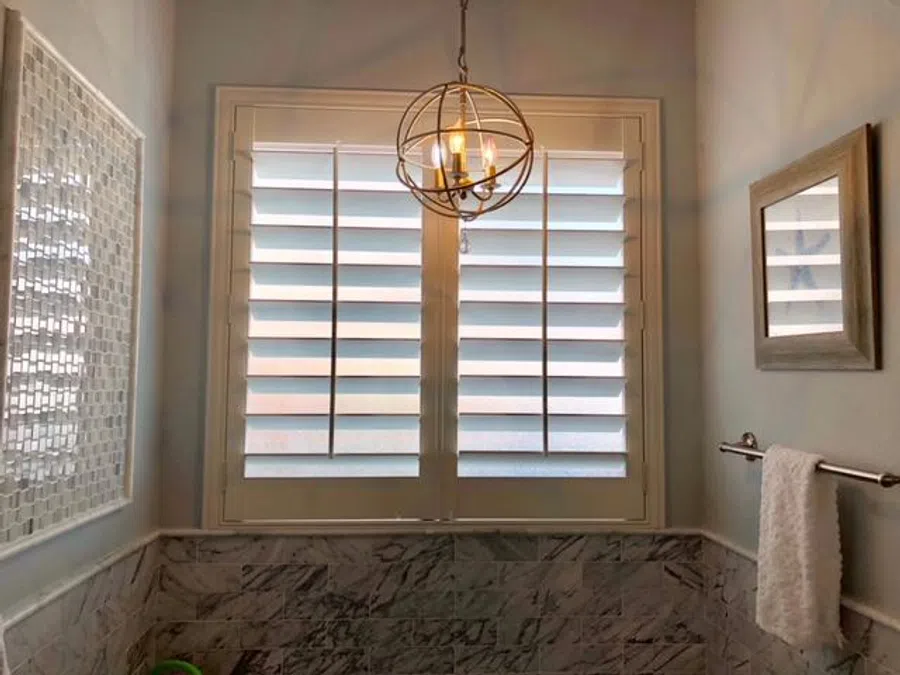 Bathroom with marble tiles, white shutter windows, chandelier, towel rack, and a framed mirror