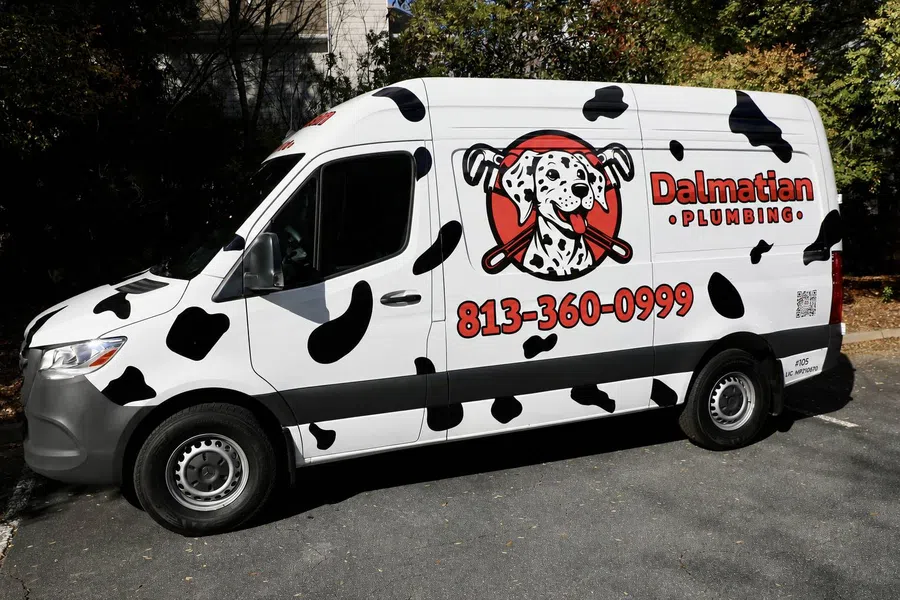 White plumbing van with black spots and Dalmatian Plumbing logo featuring a spotted dog and phone number 813-360-0999.