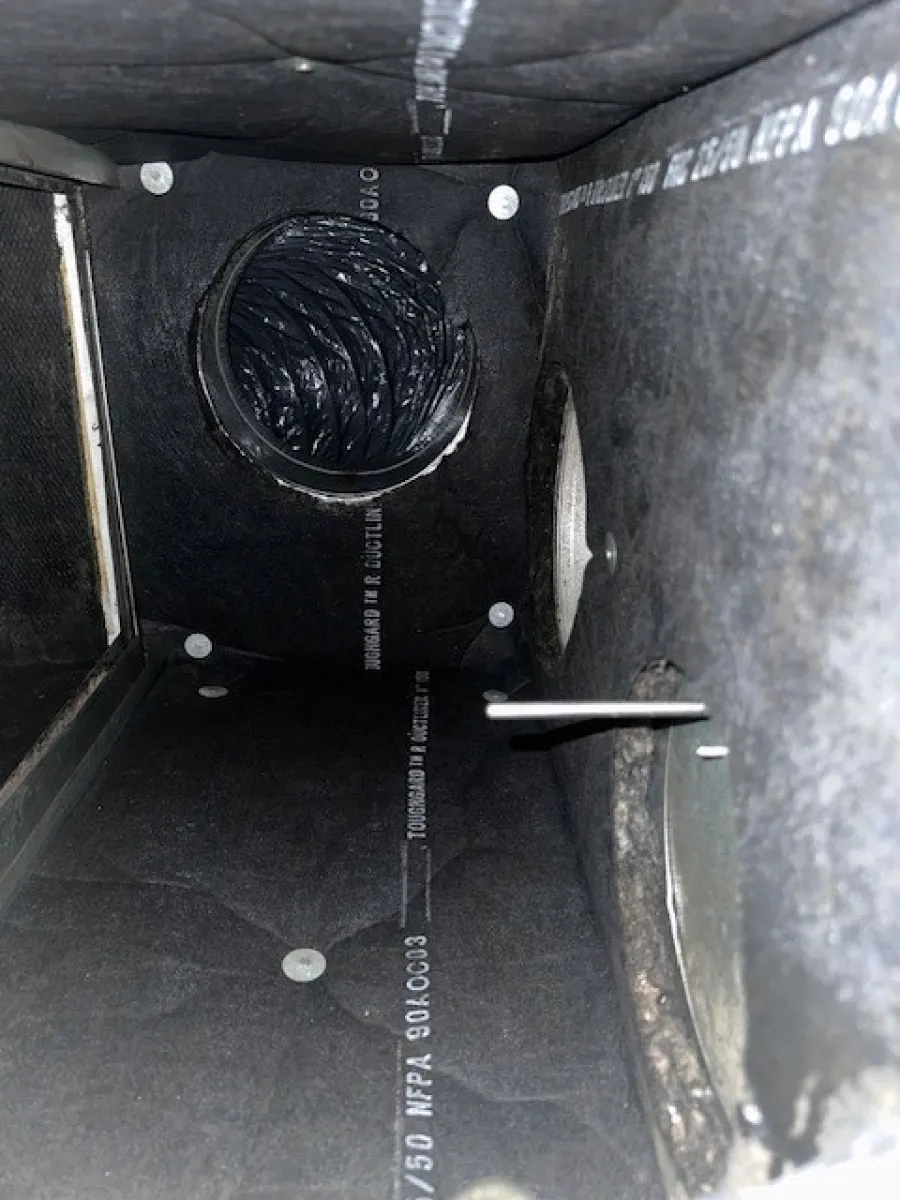 Inside view of a rectangular ventilation duct with an attached flexible black air duct inside a metal enclosure.
