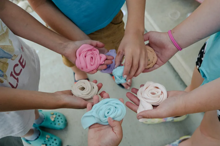 Children holding colorful swirls of homemade slime in their hands outdoors on concrete patio.