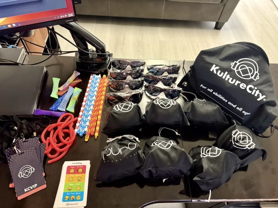 KultureCity sensory kit includes noise-canceling headphones, sunglasses, fidget toys, and calming tools on a table.