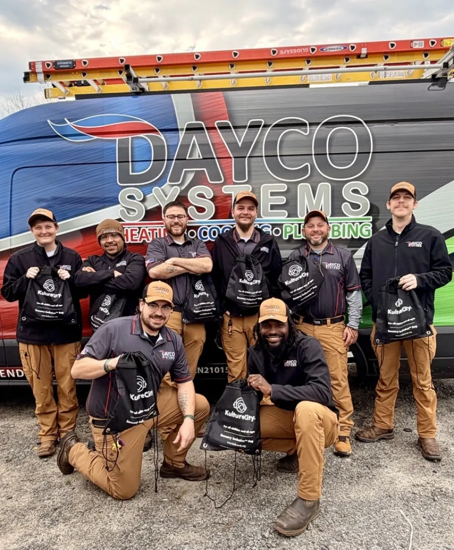 Dayco Systems team of eight workers posing in uniform in front of company van with ladders on top.