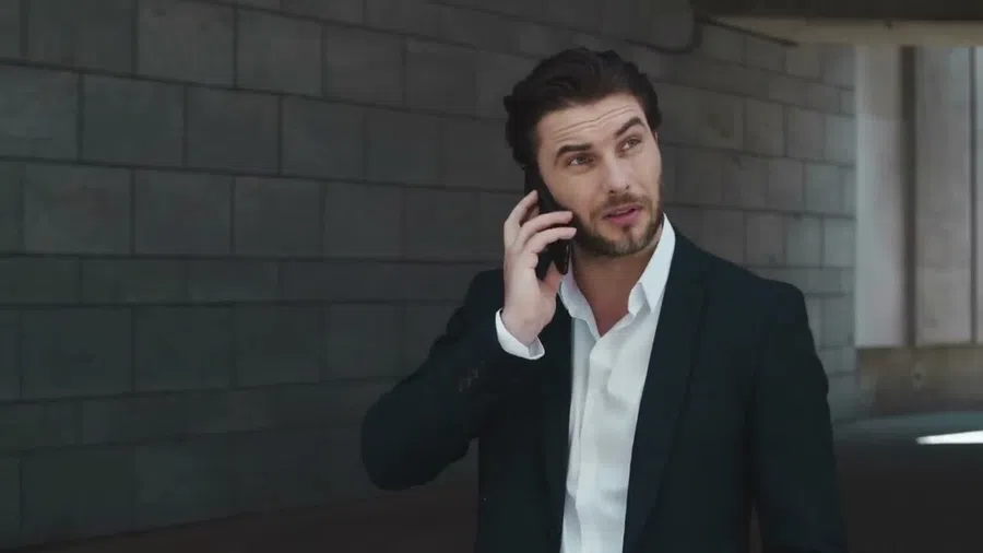 Man in black suit talking on smartphone near modern building with gray brick wall background