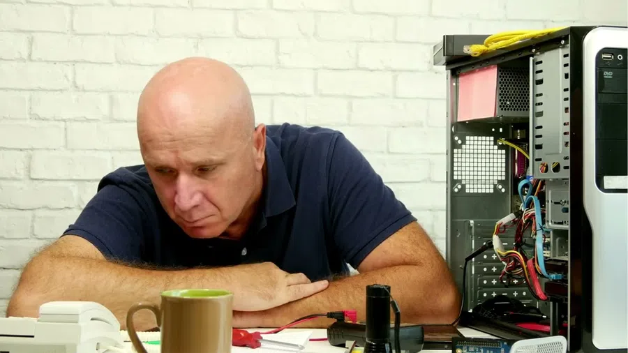 Man inspecting a disassembled desktop computer on a table with tools and a coffee cup nearby.