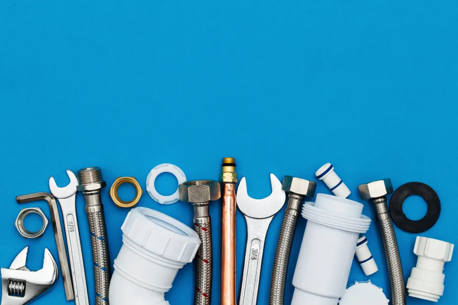 Various plumbing tools and fittings arranged on a blue background including wrenches, pipes, and connectors.