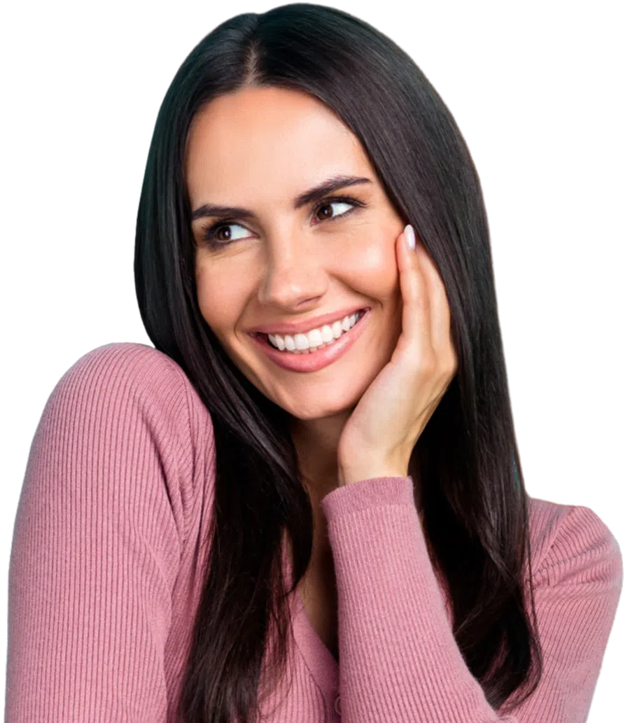 Smiling woman with long dark hair wearing a pink ribbed sweater, touching her face and looking to the side.