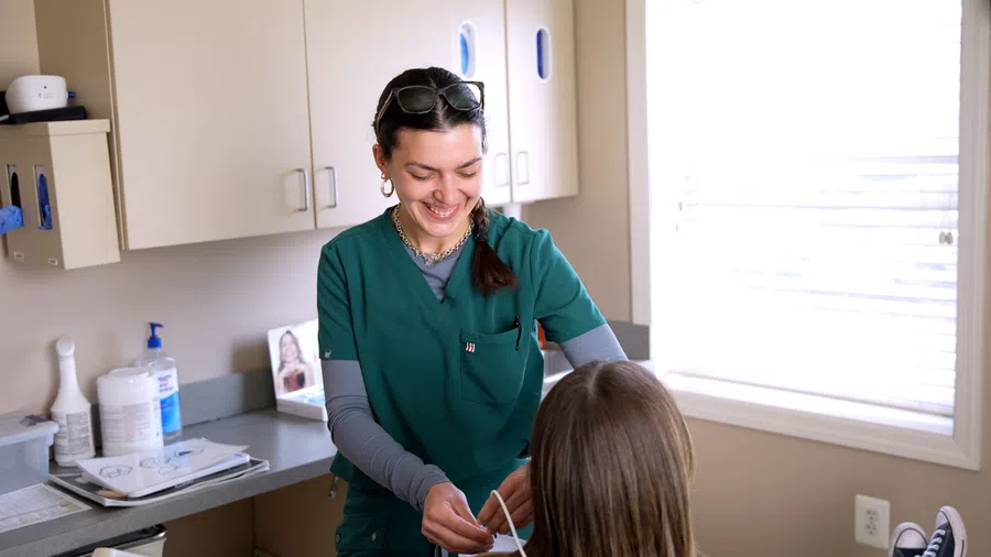 Healthcare professional in green scrubs assisting a patient with a mask in a bright medical office.