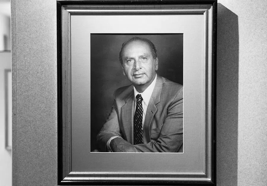 Black and white framed portrait of a man in a suit and tie with arms crossed.