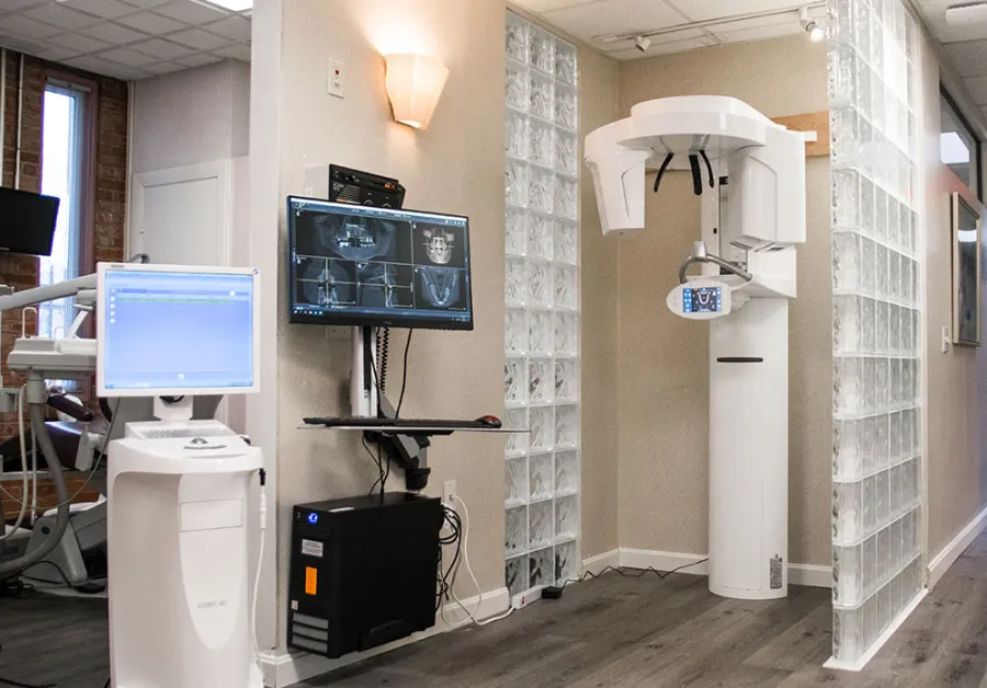 Dental office with advanced imaging equipment including a panoramic X-ray machine and computer monitors displaying dental scans.