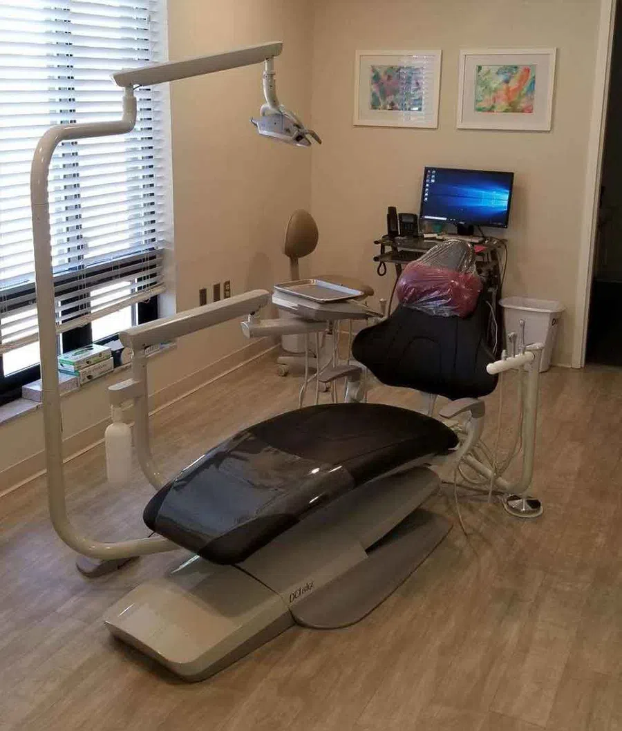 Modern dental office with black patient chair, overhead light, computer workstation, and beige walls.