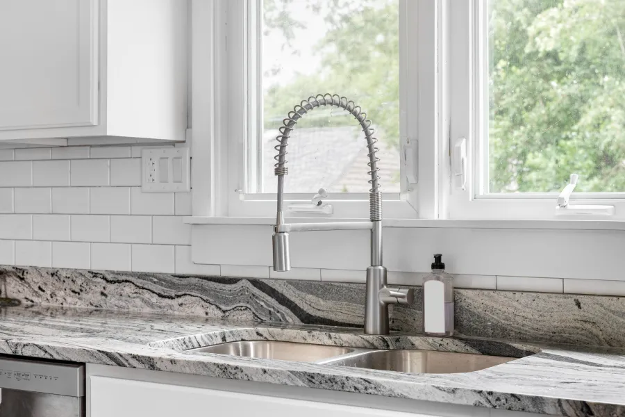 Modern kitchen sink with stainless steel faucet and granite countertop in bright white kitchen.