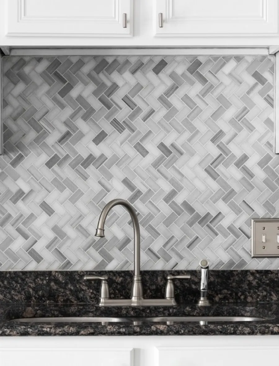 Modern kitchen sink with brushed metal faucet and gray herringbone tile backsplash under white cabinets
