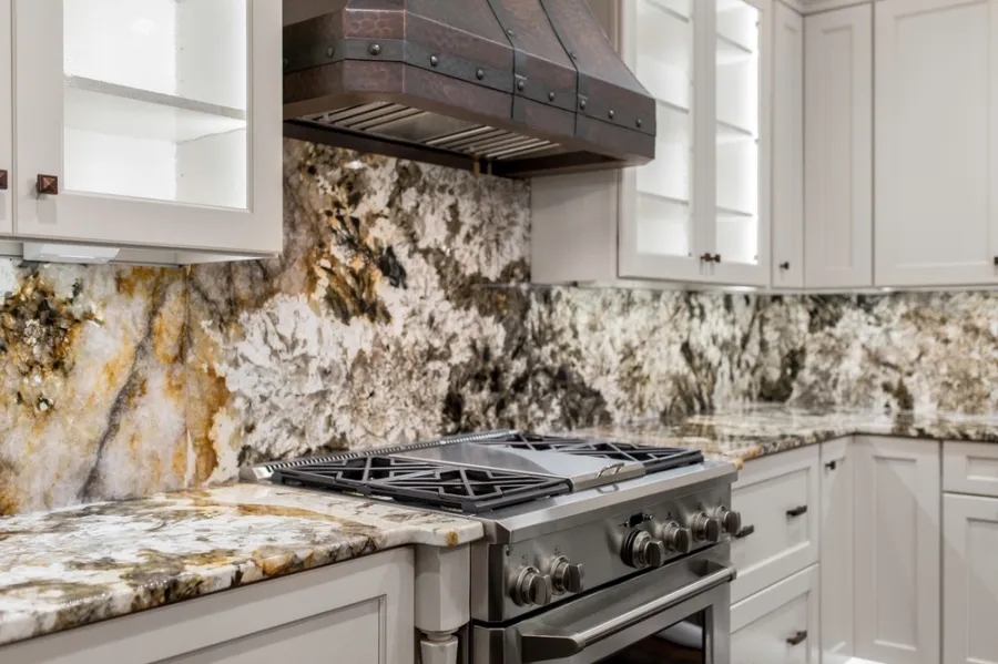 Modern kitchen featuring a stainless steel stove, rustic range hood, and granite countertops with matching backsplash.