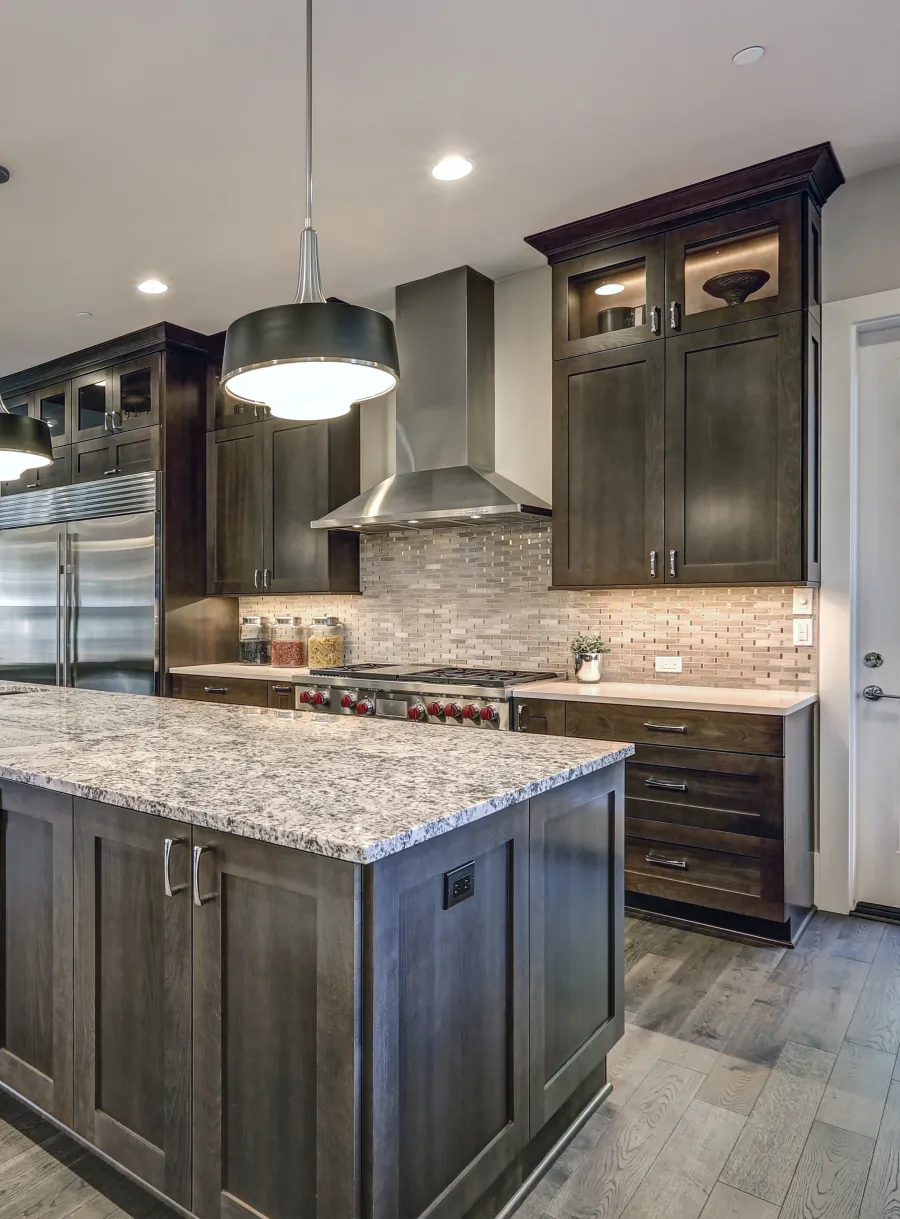 Modern kitchen with dark wood cabinets, granite island, stainless steel appliances, and pendant lighting.