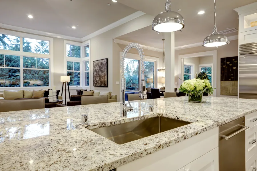 Modern kitchen with granite island countertop, stainless steel sink, pendant lights, and open living area.