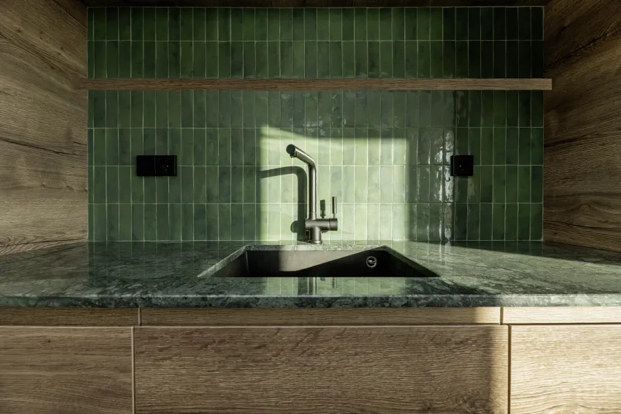 Modern kitchen sink with green tiled backsplash and wooden cabinetry under natural light.