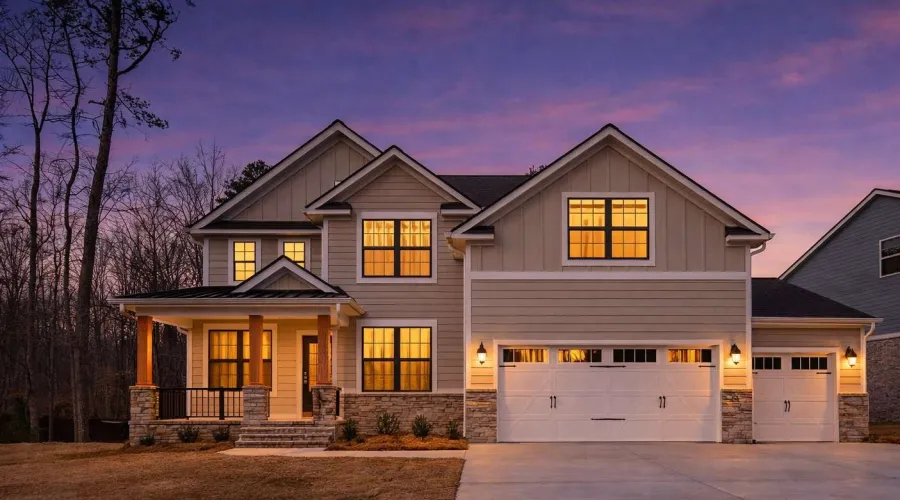Two-story modern house with lit windows, stone accents, large garage, and a twilight sky backdrop.