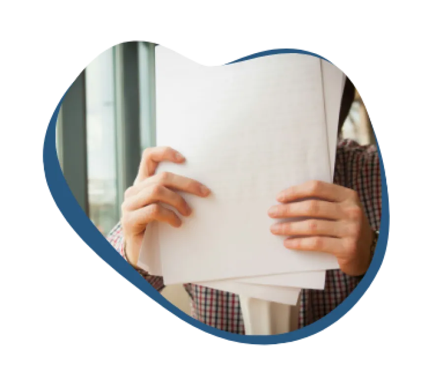 Person holding and reviewing several sheets of paper in a bright room by a window.