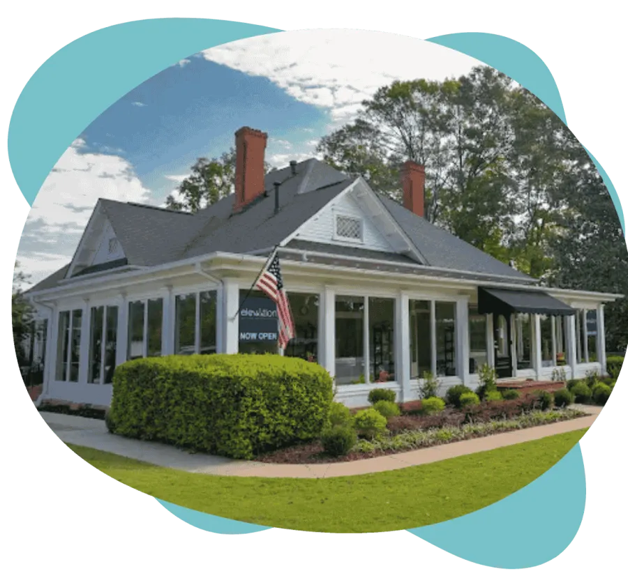 White house with large windows, American flag, manicured bushes, and a 'Now Open' sign on a sunny day.