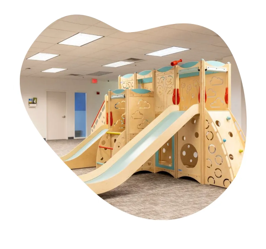 Indoor wooden playground structure with slides, climbing walls, and colorful accents in a bright playroom.
