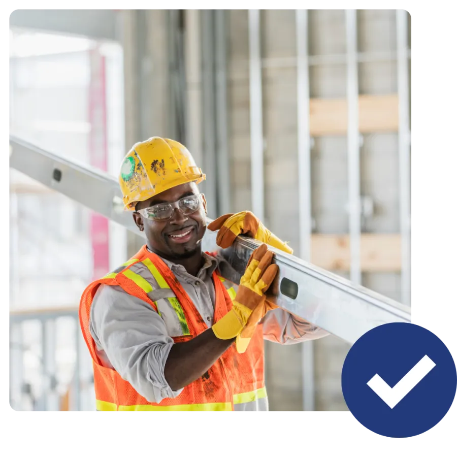 Smiling construction worker wearing safety gear holding a metal beam inside a building under construction.